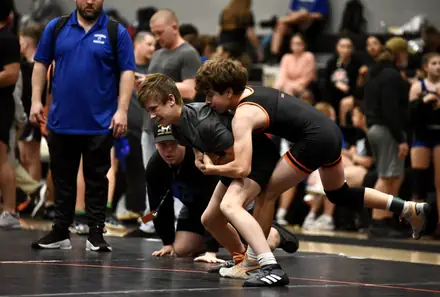 Two AWC wrestlers in club singlets compete as a coach watches from the corner
