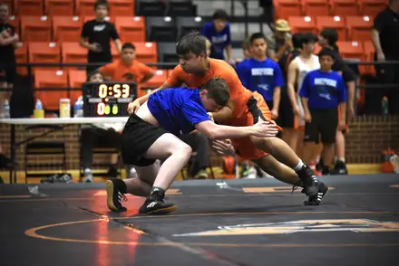 A wrestler drives through a takedown with the match clock running