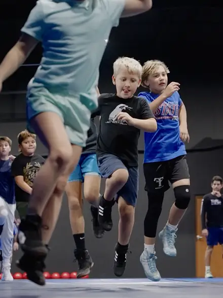 Young wrestlers jumping through a warm-up drill before practice.