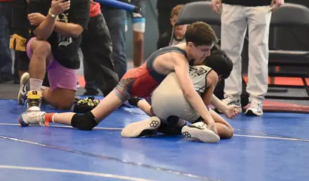 Young wrestlers competing on the mat as coaches watch from the sideline