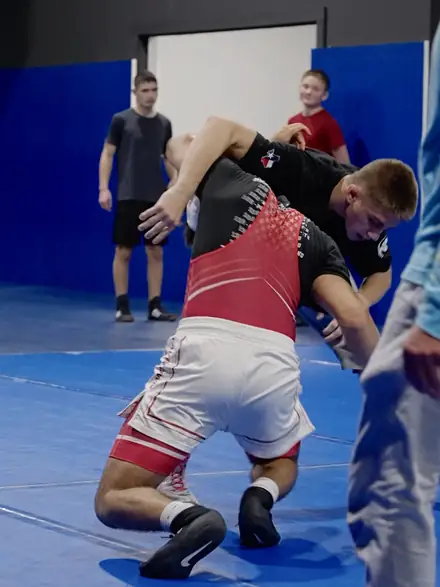 Two high school wrestlers drilling a body lock on the blue mat.