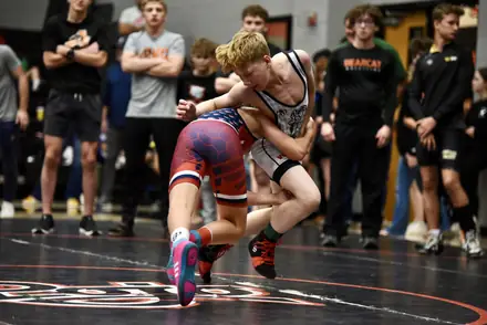 A wrestler shoots in on a leg attack as teammates watch from the mat's edge