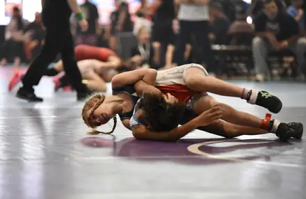 Two young wrestlers scramble for control at the edge of the mat
