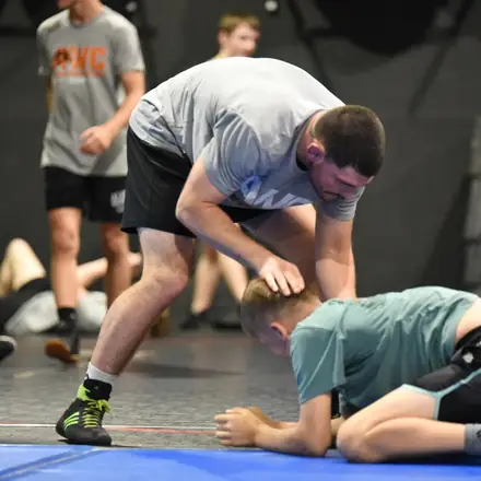 A coach walking a wrestler through a pinning position on the mat.