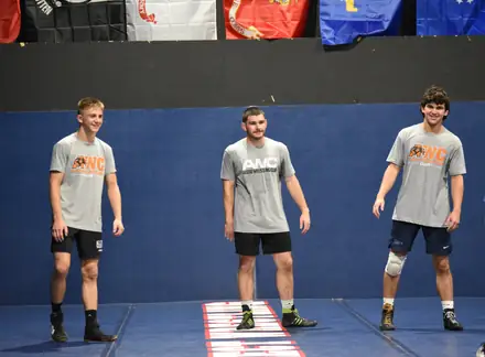 Three AWC wrestlers in club shirts standing on the mat before a session