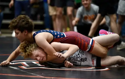A young wrestler in a stars and stripes singlet locks up a turn on the mat
