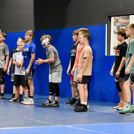 A group of young wrestlers lined up along the edge of the mat waiting for their turn.