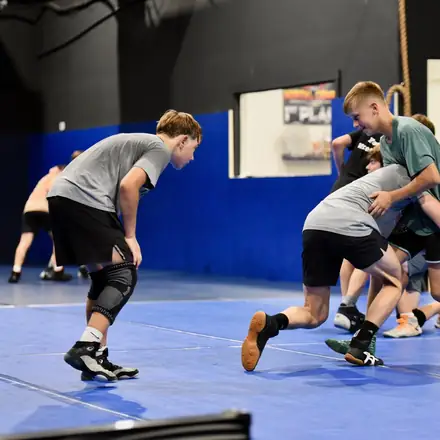 A coach directing a drill while wrestlers work in pairs.