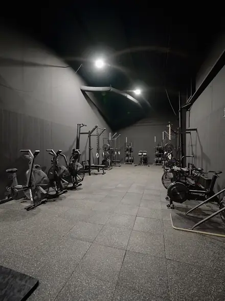 A long view down the weight room, racks and conditioning bikes lining the wall.