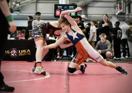 A wrestler sprawls on a shot during a match on the red competition mat