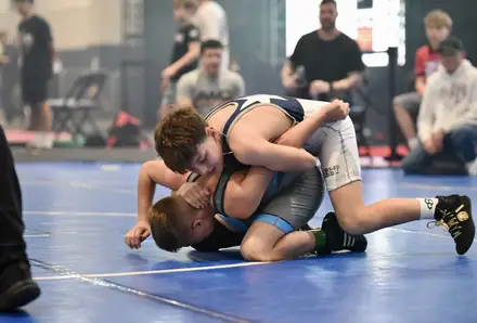 An AWC wrestler controls an opponent on the blue tournament mat