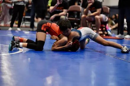 An AWC wrestler in orange and black works a tilt on the blue competition mat