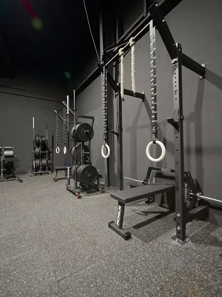 The club weight room, with squat racks, gymnastic rings and bumper plates.