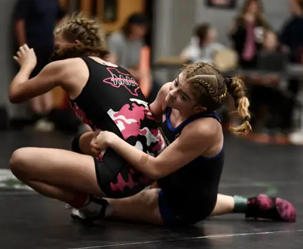 Two girls grapple on the mat during a competitive youth match