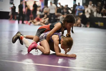 A girl works for position on a purple competition mat as spectators watch from the sidelines