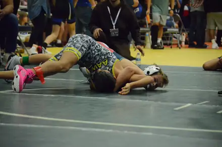 Two wrestlers battle on the yellow competition mat