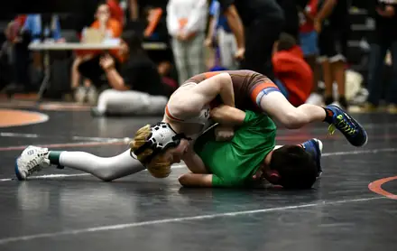 Two wrestlers battle on the mat with the crowd watching behind them