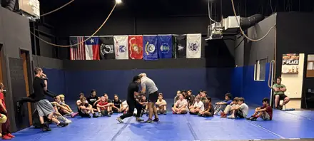 Coaches talking to the team seated on the mat at the start of practice