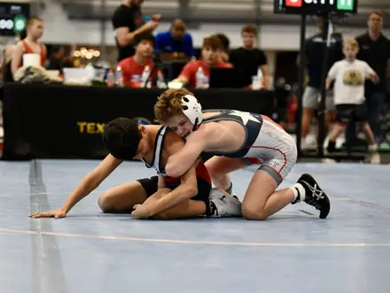 A wrestler works for the fall on the blue competition mat