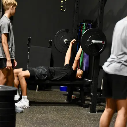 A lifter pressing under the bar while a coach spots the set.
