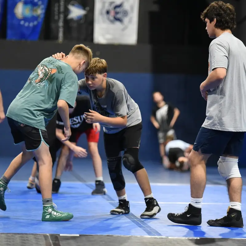 A coach demonstrating an underhook on a partner while the rest of the room watches.