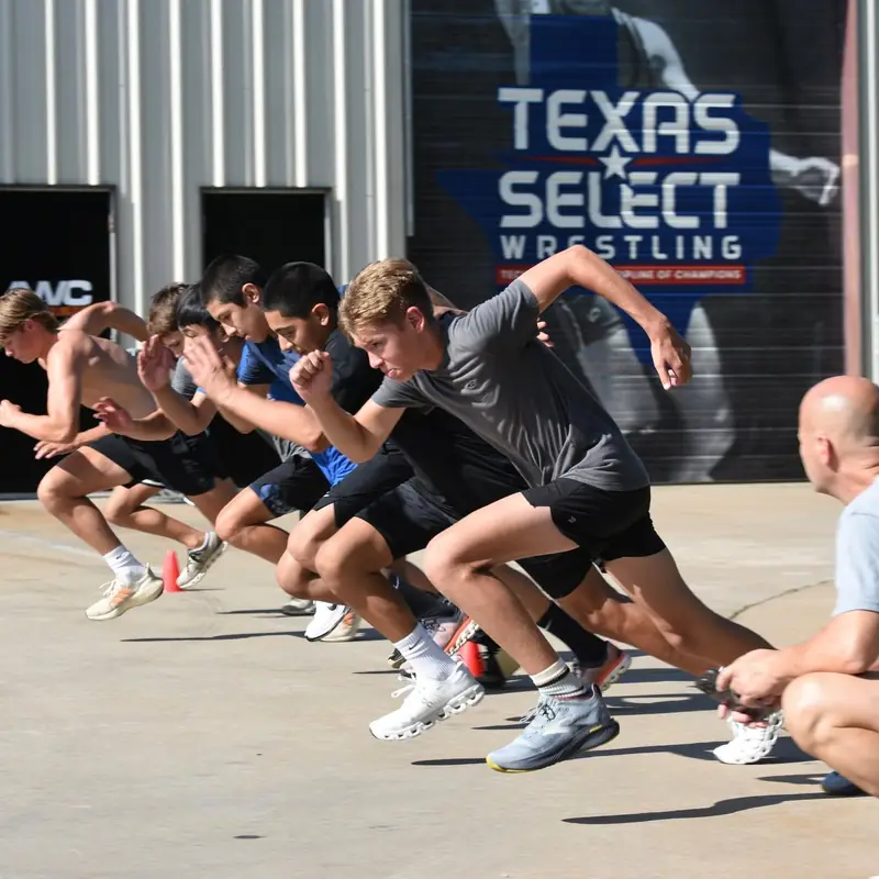 A long line of AWC wrestlers driving forward in a sprawl drill beneath the Texas Select Wrestling banner.