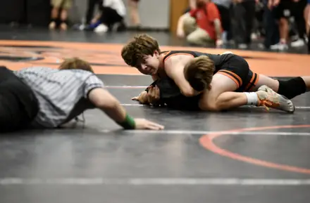 A wrestler turns an opponent toward his back as the official drops to check