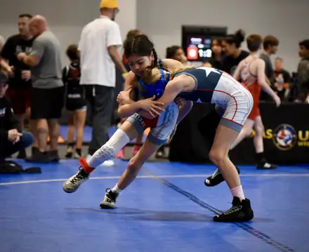 A girl attacks a leg during a match on the blue competition mat