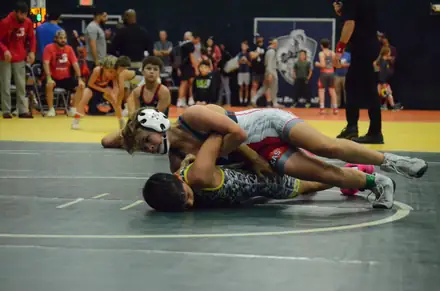 Two wrestlers in headgear grapple for control during a match