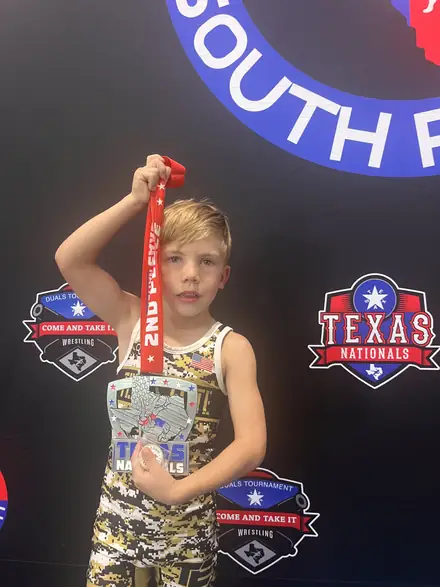 An AWC wrestler holding up a second-place medal at the Texas state backdrop