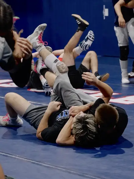 Wrestlers drilling bridges and back exposure across the blue mat.
