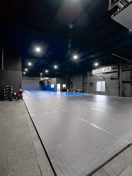 The full training floor, roll-out mats stacked along the far wall.