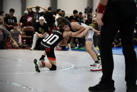 A wrestler drives through a takedown as the official moves in to watch the action