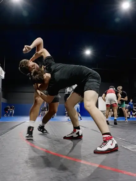 Two high school wrestlers wrestling live beneath the gym lights.