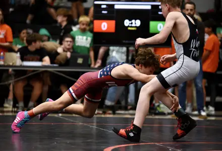 A wrestler shoots in with the match clock counting down behind them