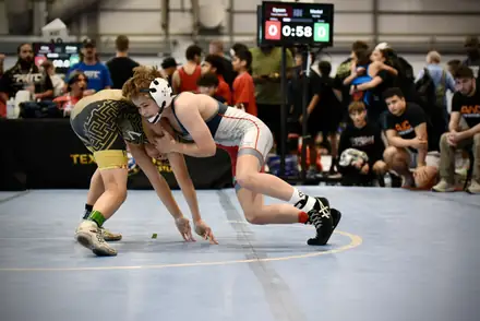 Two wrestlers scramble for control on the blue tournament mat