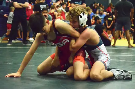 Young wrestlers competing on the mat in front of a packed crowd