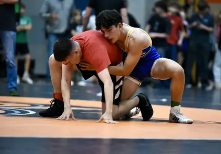 A wrestler pushes the pace against an opponent on the blue mat