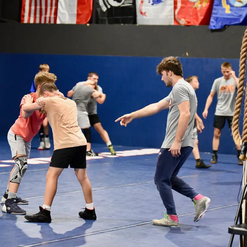Young AWC wrestlers drilling takedowns in pairs across the mat.