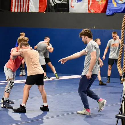 Young AWC wrestlers drilling takedowns in pairs across the mat.