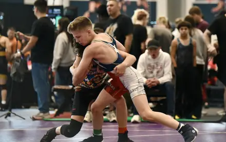 A wrestler drives an opponent across the mat during a match
