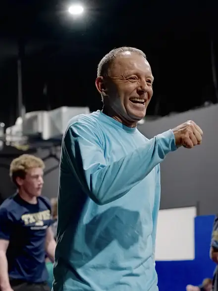 A coach laughing while showing a hand position to the room.