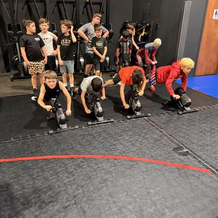 A line of athletes driving weighted sleds down the turf lane.