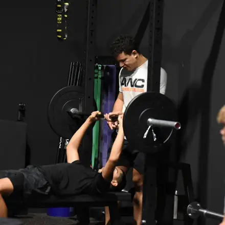 An AWC athlete bench pressing with a spotter standing over the bar.