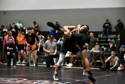 A wrestler is lifted off his feet mid-throw during a tournament bout
