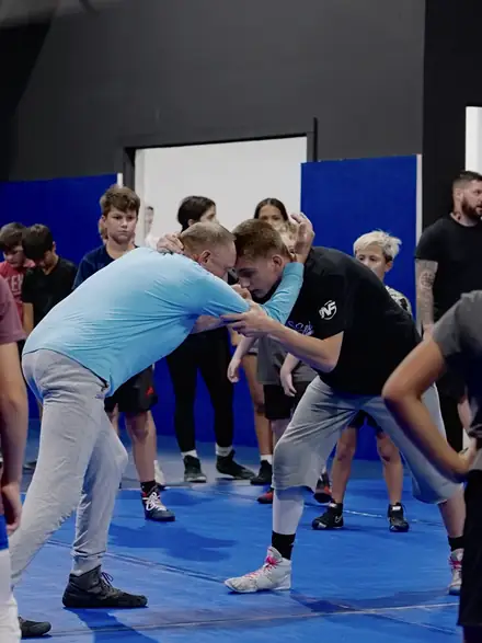 A coach setting up a takedown on a young wrestler while the room watches.