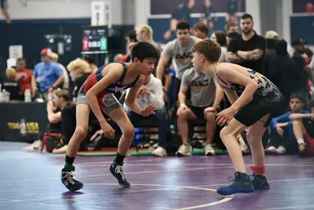 Three wrestlers in their stances at the center of the tournament mat