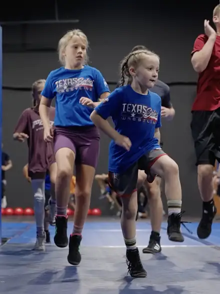 Young wrestlers in Texas Select shirts running a warm-up lap around the mat.
