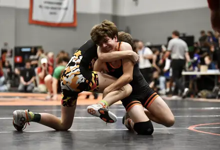 Two wrestlers tie up at the center of the mat during a match