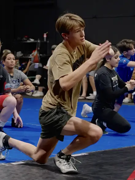 A wrestler dropping into a low stance during a warm-up drill.